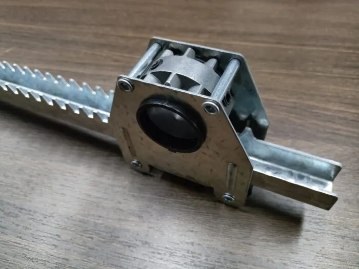 Pinion housing engaged with straight toothed gear rack, showing tooth form and guide rollers